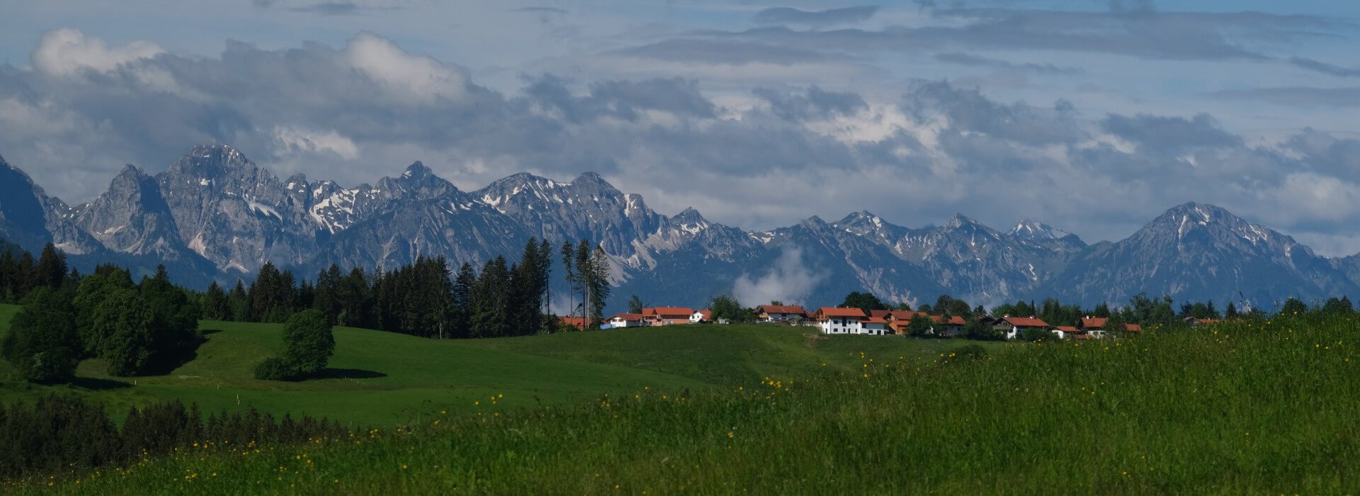 Im Hintergrund sind die Alpen zu sehen und im Vordergrund liegt sehr idyllisch die Gemeinde Wildsteig umrahmt von grünen Wiesen