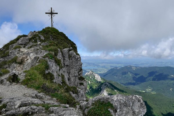 Bergipfel mit Gipfelkreuz. Im Hintergrund das Alpenvorland.