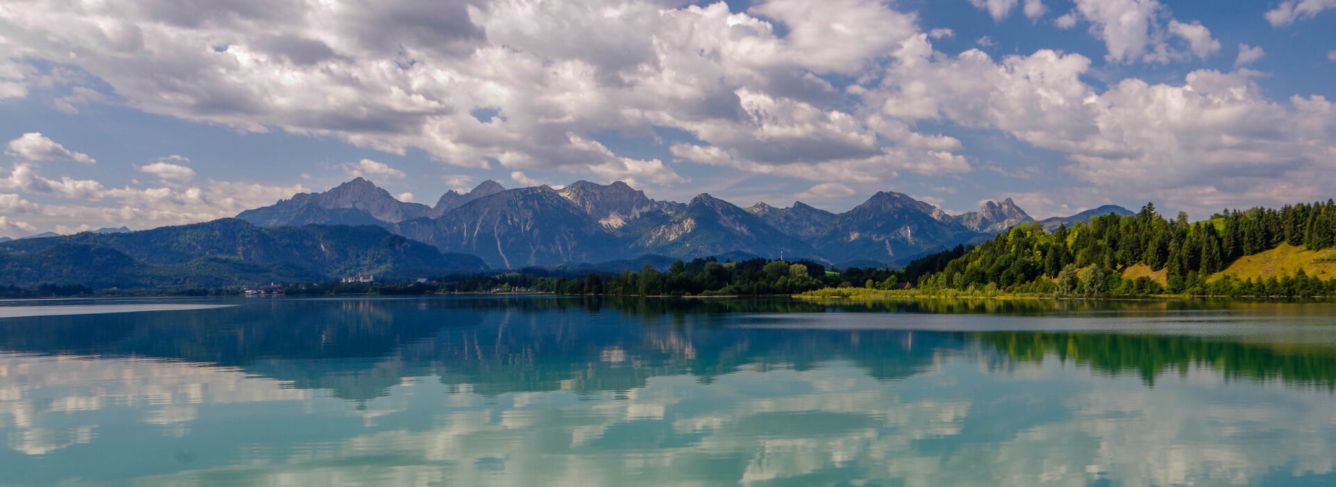 Blick auf den Forggensee Richtung Füssen und die Alpen an einem sonnigen Tag.