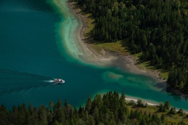 Luftaufnahme des Plansees mit einem Ausflugsboot auf tükisblauem Wasser.